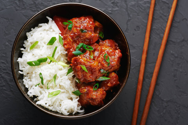 Κοτόπουλο Manchurian σε μπολ με ρύζι μπασμάτι σε μαύρο μπετόν φόντο. Κοτόπουλο Manchurian είναι ινδική κινεζική κουζίνα πιάτο με στήθος κοτόπουλο, πιπεριά, ντομάτες, σάλτσα σόγιας. - Φωτογραφία, εικόνα
