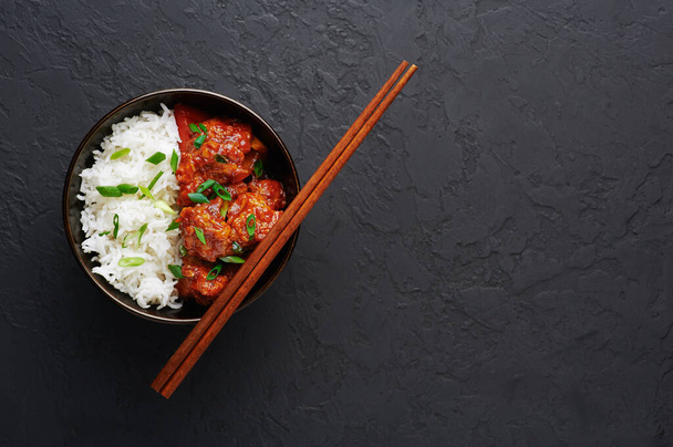 Kana Mantsurian kulhoon basmatiriisi mustalla betonitaustalla. Kana Mantsuria on intialainen kiinalainen ruokalaji, jossa on kananrintoja, paprikaa, tomaatteja, soijakastiketta. Kopioi tila - Valokuva, kuva