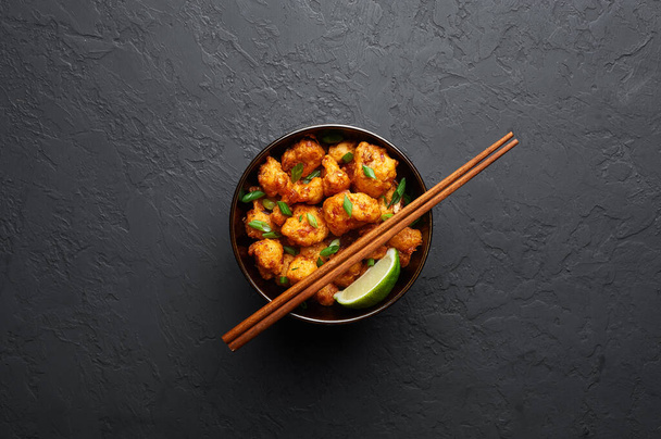 Gobi Manchurian in bowl at black concrete background. Gobi Manchurian is Indian Chinese cuisine dish with cauliflower, tomatoes, onion, soy sauce. Copy space - Photo, Image