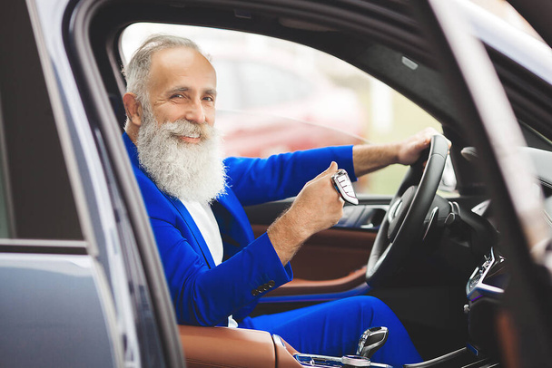 Old stylish man in car sales center. Mature man choosing new automobile. - Foto, afbeelding