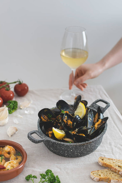 Medditeranean lunch, fresh cooked mussels with tomato, parsley, lemon, fresh bread and white wine on a table - Photo, image