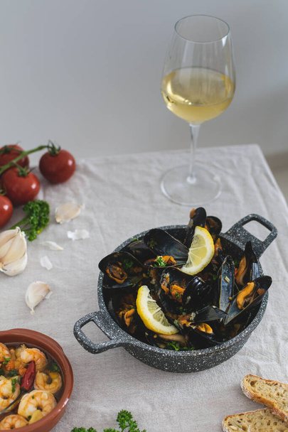 Μεσογειακό γεύμα, φρέσκα μαγειρεμένα μύδια με ντομάτα, μαϊντανό, λεμόνι, φρέσκο ψωμί και λευκό κρασί σε ένα τραπέζι - Φωτογραφία, εικόνα