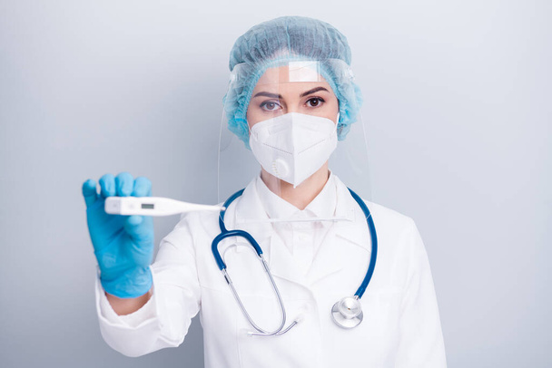 Closeup photo of serious infection disease virologist doctor hold thermometer border control wear coat respirator mask facial plastic protection surgical hat gloves isolated grey background - 写真・画像