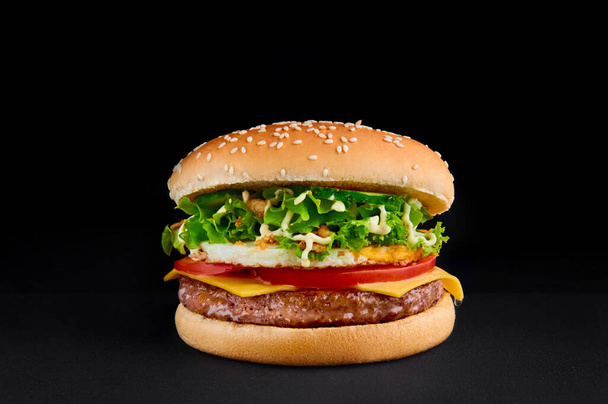 perfekte Burger mit Schnitzel, Käse, Tomate, Salat, Omelette, isoliert auf schwarzem Hintergrund Kopierraum - Foto, Bild