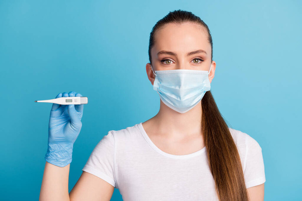 Closeup photo of beautiful lady hospital examination doctor hold thermometer hand show body temperature patient wear protect face medical mask white t-shirt isolated blue color background - Φωτογραφία, εικόνα