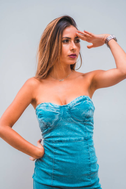 Lifestyle session, a young caucasian brunette in a blue denim dress on a plain gray background, looking to the right - Foto, Imagen