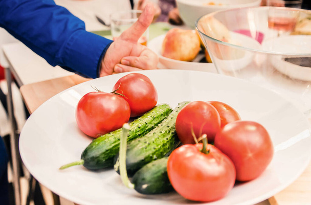 Кухар показує "відмінний" жест, піднімає великий палець вгору. На передньому плані помідори та огірки на тарілці
 - Фото, зображення