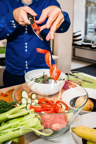 Ruce házejí nakrájená rajčata do mísy zeleniny. Kuchař připraví řecký salát - Fotografie, Obrázek