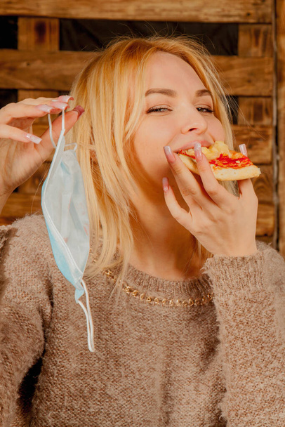 Keep calm and bon appetit! Young bold beautiful woman eating pizza without medicine respirator mask. - Photo, Image