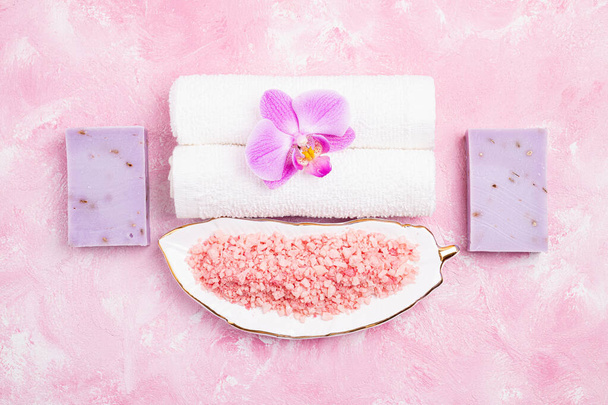 Spa behandeling wellness concept. Natuurlijke spa cosmetica producten, accessoires, zeep, zeezout, tropische bloem op roze achtergrond. Spa achtergrond plat lay. Bovenaanzicht - Foto, afbeelding