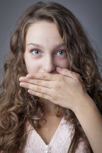 De mond van een jonge mooie vrouw sluit met haar hand als symbool van bedrog en manipulatie.  - Foto, afbeelding