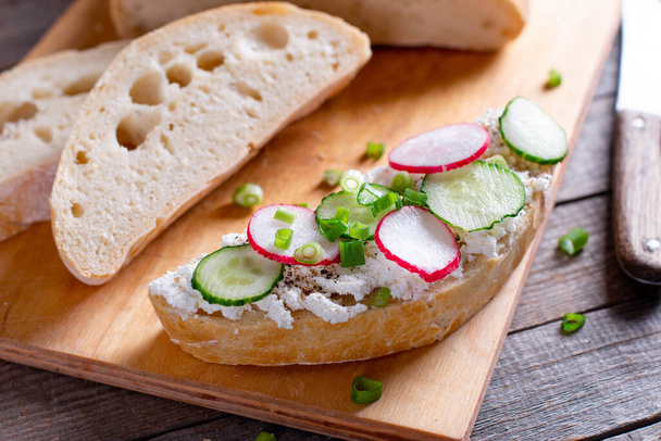 бутерброди з огірками, редькою та вершковим сиром на дерев'яній дошці, крупним планом, концепція сніданку або обіду
 - Фото, зображення