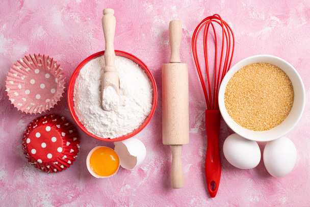 Ainesosat leivontaan - jauhot, munat, sokeri vaaleanpunaisella pohjalla. Leivonta tai ruoanlaitto kakkuja tai muffinsseja. Top view, tasainen lay - Valokuva, kuva
