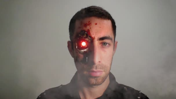 Cinemagraph of dramatic closeup portrait of a young bearded man with an expressionless face and revealed half cyborg humanoid face looking at the camera. He is with serious facial expressions. Loop. - Footage, Video