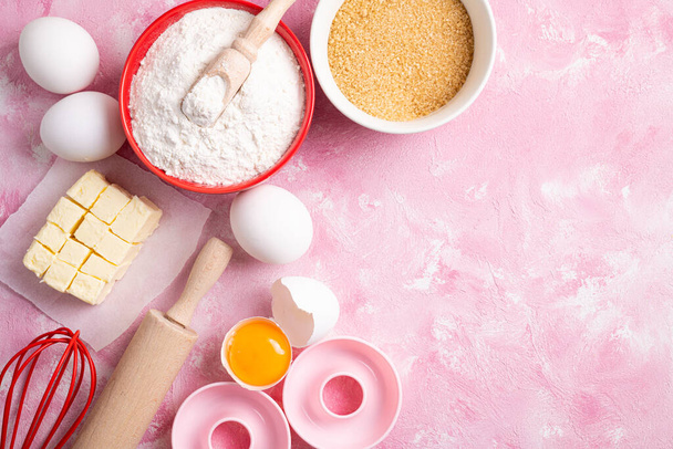 Ingrédients pour cuire la farine, les œufs, le beurre, le sucre sur fond rose à plat. Cuisson ou cuisson de gâteaux ou de beignets. Fond de cuisson. Vue du dessus, espace de copie
 - Photo, image