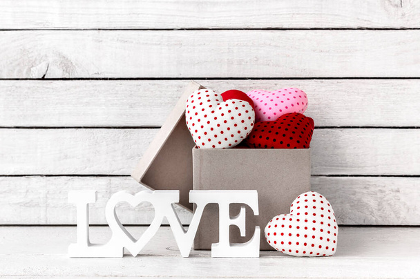 Mnoho červené srdce tvarované s hnědé dárkové krabice a láska abeceda přes bílé dřevo pozadí - Fotografie, Obrázek