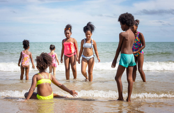 Παιδιά που παίζουν τρέξιμο στην άμμο στην παραλία, μια ομάδα παιδιών που κρατιούνται χέρι-χέρι σε μια σειρά στην παραλία το καλοκαίρι, πίσω όψη ενάντια στη θάλασσα και τον γαλάζιο ουρανό - Φωτογραφία, εικόνα