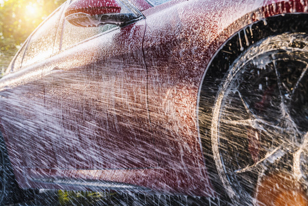 Rozstřikování pěny na červené sportovní auto s vysokotlakou pěnou zbraň mytí aut v mytí aut - Fotografie, Obrázek