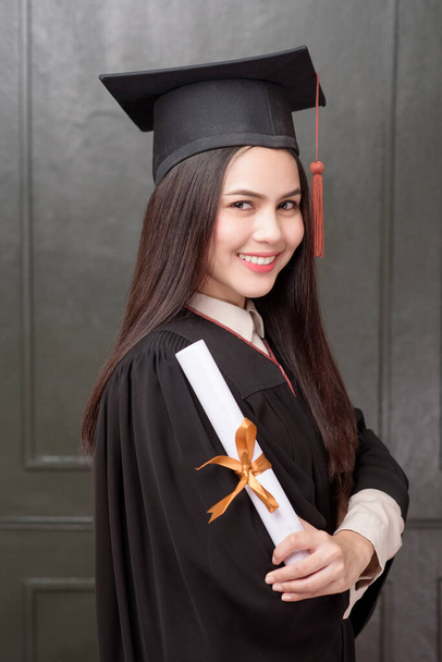 Portrait of young woman in graduation gown smiling and cheering on black background  - Fotoğraf, Görsel