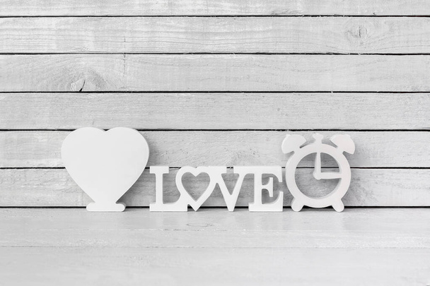 Corazón blanco en forma de alfabeto de amor y reloj en forma de madera blanca sobre fondo de madera blanca
 - Foto, Imagen
