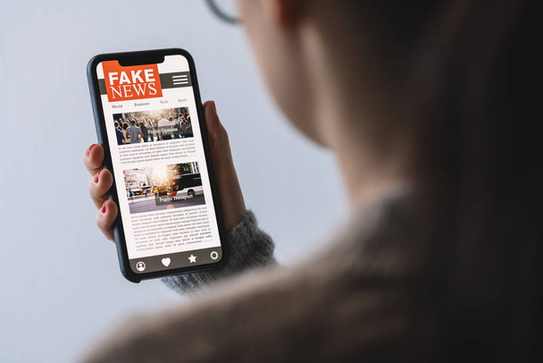 Online fake news on a mobile phone. Close up of woman reading Fake news HOAX or articles in a smartphone screen application. Hand holding smart device. Mockup website. Fake Newspaper portal. - Fotoğraf, Görsel