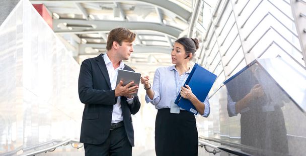 Έννοια της εταιρικής σχέσης στις επιχειρήσεις. Νεαρός άντρας και γυναίκα μιλάνε για δουλειές ενώ περπατούν στο πεζογέφυρα. - Φωτογραφία, εικόνα