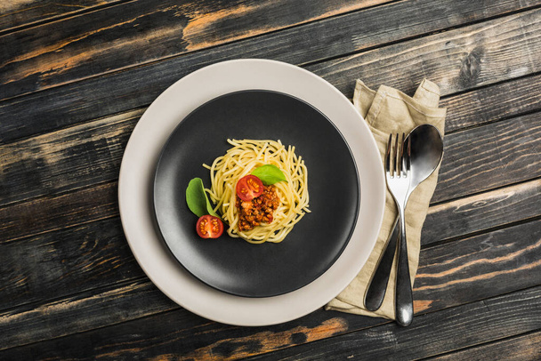 Heerlijke klassieke Italiaanse Bolognese pasta met tomaten en Basilicum op een bord op een donkere houten achtergrond. Bovenaanzicht, horizontale oriëntatie. - Foto, afbeelding
