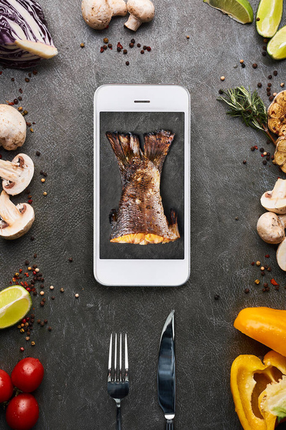 creative food concept with roasted fish tail in smartphone display. restaurant delivery concept. Gourmet cuisine. Vertical - Fotó, kép