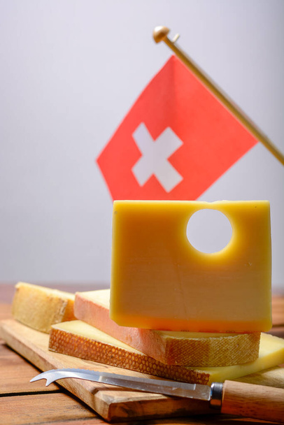 Block of Swiss Emmental or Emmentaler medium-hard cheese with round holes made from cow milk in Canton Bern with flaf of Switzerland - Photo, Image