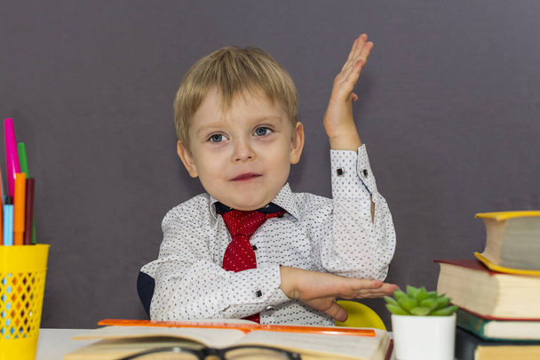 Chłopiec wyciąga rękę. przedszkolak siedzi przy biurku - Zdjęcie, obraz
