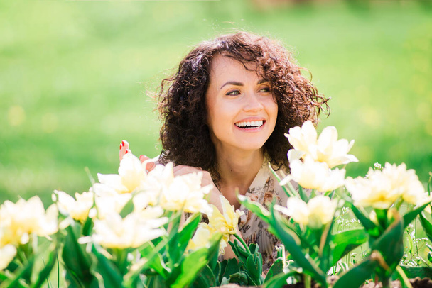 Jonge aantrekkelijke vrouw met krullend lang haar poseren in de lente bloeiende tuin - Foto, afbeelding