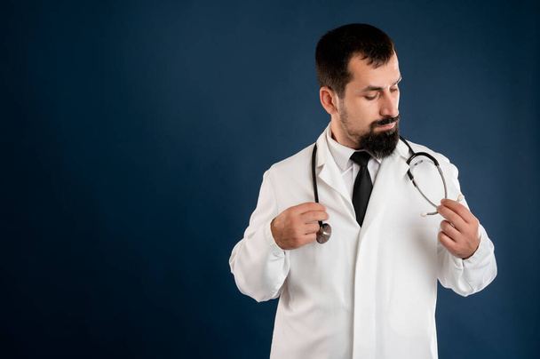 Portret lekarza z stetoskopem w mundurze medycznym układa stetoskop na niebieskim odizolowanym tle. - Zdjęcie, obraz