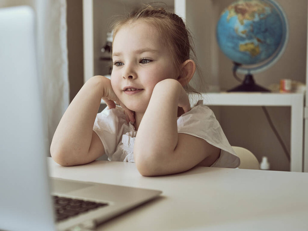 Милая маленькая девочка использует ноутбук дома. Образование, онлайн-обучение, домашнее обучение
 - Фото, изображение