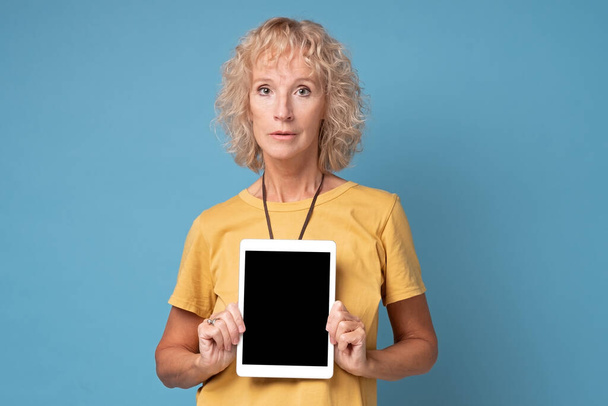 Szőke idős fehér nő mutatja üres tabletta képernyő. - Fotó, kép