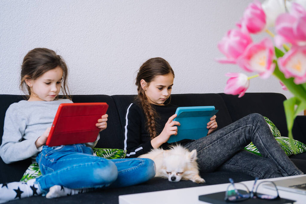 Online-Bildung, Fernunterricht, Hausaufgabenbetreuung. Kinder lernen Hausaufgaben während des Online-Unterrichts zu Hause mit Tablet oder Laptop und halten Videokassetten in der Hand. Soziale Distanz in Quarantäne. Selbstisolierung - Foto, Bild