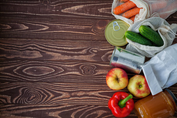 A set of different food products for home purveyance. Some of them are in reusable bags. Canned food, rice, fruits and vegetables on a wooden background. Copy-space, top view - Φωτογραφία, εικόνα