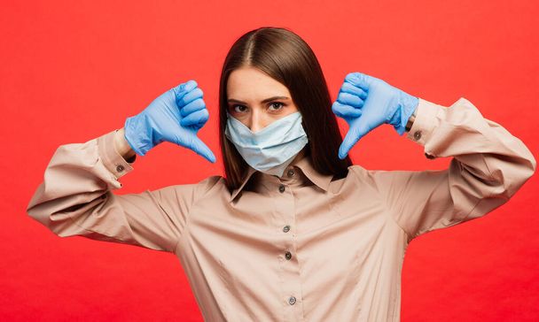 Iloinen ja iloinen nuori nainen leikkii suojaava lääketieteellinen naamio ja siniset käsineet punaisella taustalla. Lähikuva muotokuva. Sepelvaltimoviruksen karanteenin loppu, eristys. Covid-2019, pandemia 2020 - Valokuva, kuva