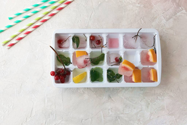 Cubos de hielo con menta, limón y bayas rojas en una bandeja para hacer bebidas, postres, alimentos saludables
 - Foto, imagen
