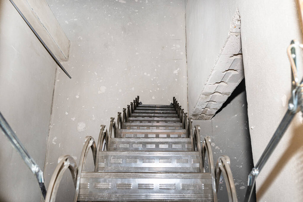 Schuivende metalen trap naar de zolder in het plafond, open klep en uitgevouwen trap, moderne uitstraling. Uitzicht vanaf de bovenkant van de trap. - Foto, afbeelding