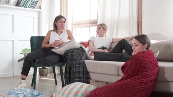 3人の女友達が話している。彼らは家に座ってコーヒーを飲む。彼らはソファに座って話をする - 映像、動画