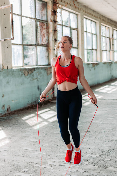 Athletic fit girl rope jumping. Fitness training, healthy lifestyle. Indoors shot in an old building - Fotó, kép