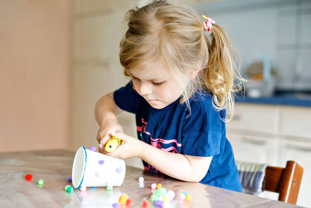 Pikkulapsi tyttö tekee veneet lyhty paperimukeja, värikkäitä pompompompompoja ja liimaa aikana pandemian koronaviruksen karanteenitauti. Onnellinen luova lapsi, kotiopetus ja kotihoito vanhempien kanssa - Valokuva, kuva