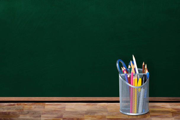 Koncepcja "powrót do szkoły" w pustej sali lekcyjnej pokazująca posiadacza ołówka i stacjonarne przedmioty na stole z przestrzenią do kopiowania na tablicy. - Zdjęcie, obraz