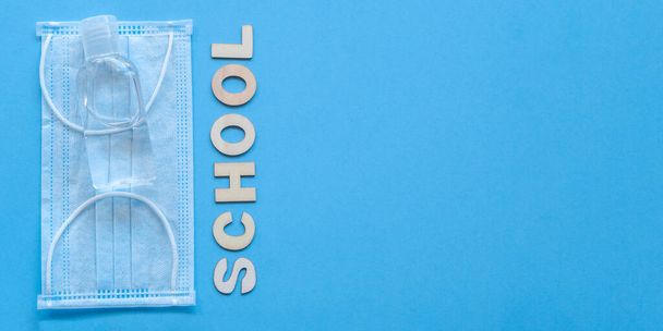 Study flatly concept. Education process after coronovirus with medical mask and sanitizer on blue background, back to school or kindergarten. summertime and learn. Woody school inscription, banner. - Photo, Image