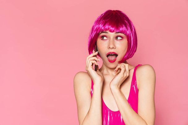 Image of young beautiful girl wearing wig talking on cellphone isolated over pink background - Fotó, kép