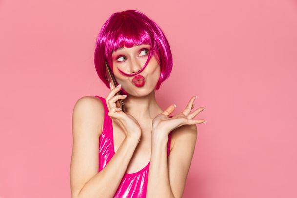 Image of young beautiful girl wearing wig talking on cellphone isolated over pink background - Photo, image