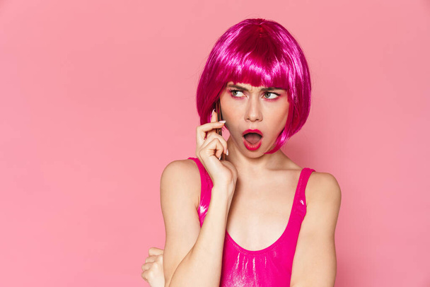 Image of young beautiful girl wearing wig talking on cellphone isolated over pink background - Photo, Image