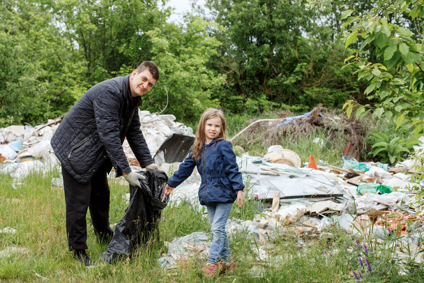 a middle-aged man, a father and his daughter are putting garbage in a black bag - Фото, зображення