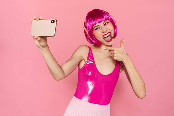 Image de femme joyeuse dans le casque pointant du doigt et prenant selfie sur téléphone portable isolé sur fond rose
 - Photo, image