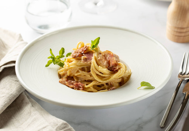 Pasta carbonara served in deep white plate with oregano - Foto, afbeelding